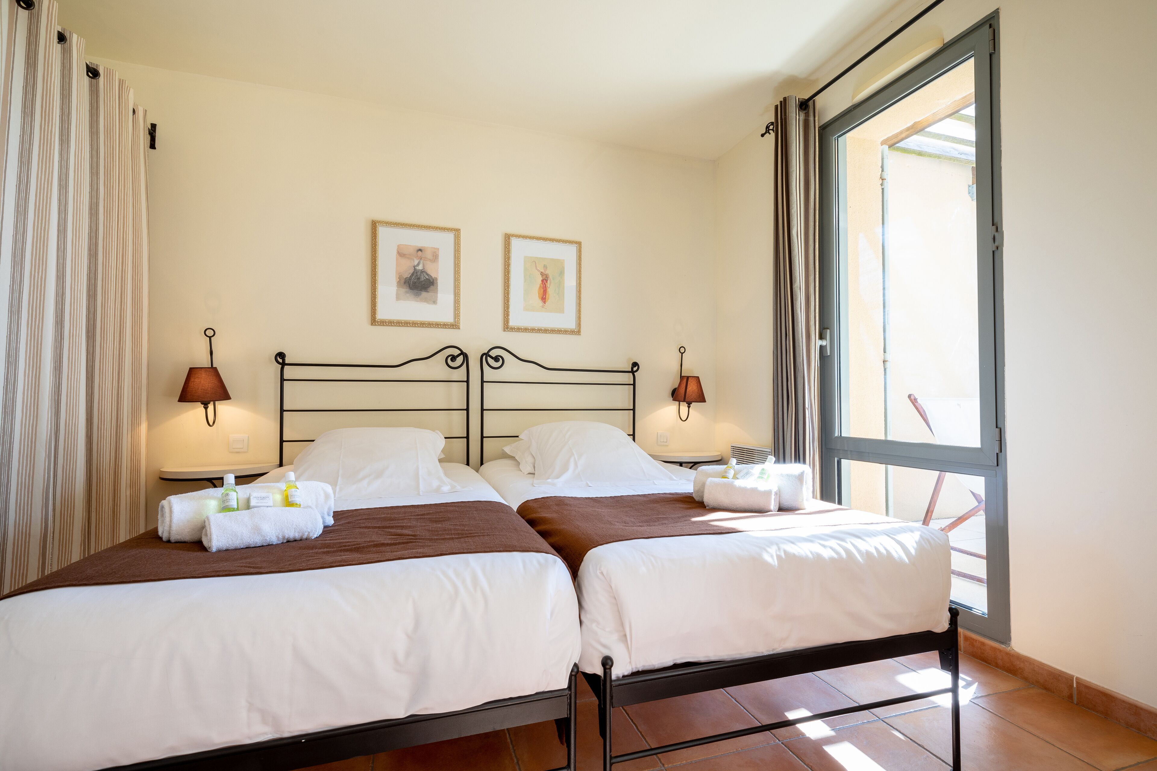 Una habitación de hotel con dos camas, un ventanal grande y dos cuadros en la pared.