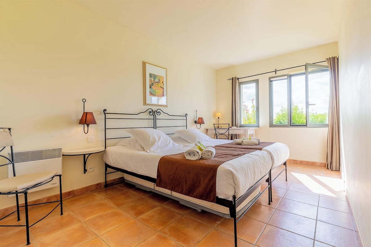 A bedroom with a bed, two bedside tables, a chair, a window with curtains, and a painting on the wall.
