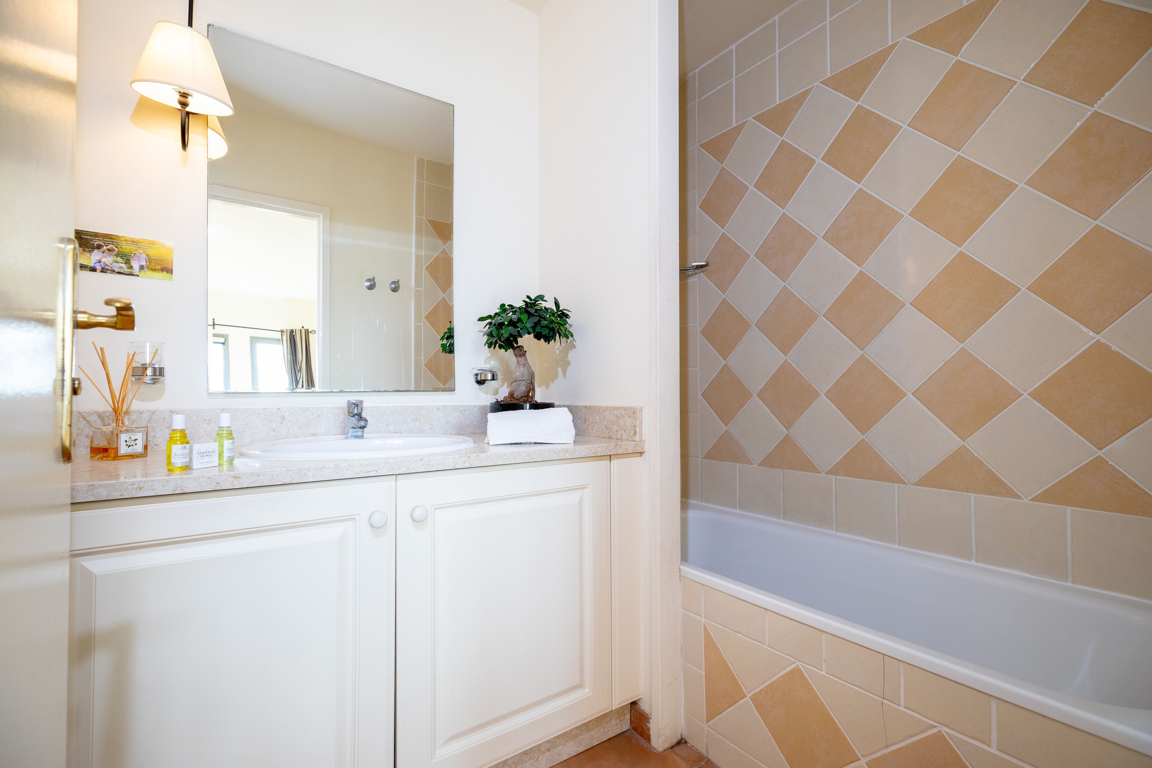 A bathroom with a white sink, mirror, and a shower with beige diamond-patterned tiles.