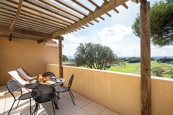 Un espacio de comedor al aire libre con techo, una mesa y sillas, y vistas a un campo de golf, además de una pérgola.