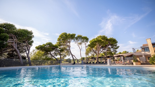 A swimming pool with clear blue water, surrounded by trees and a building with outdoor seating. - Le Domaine de Provence Country Club (Saumane-de-Vaucluse)