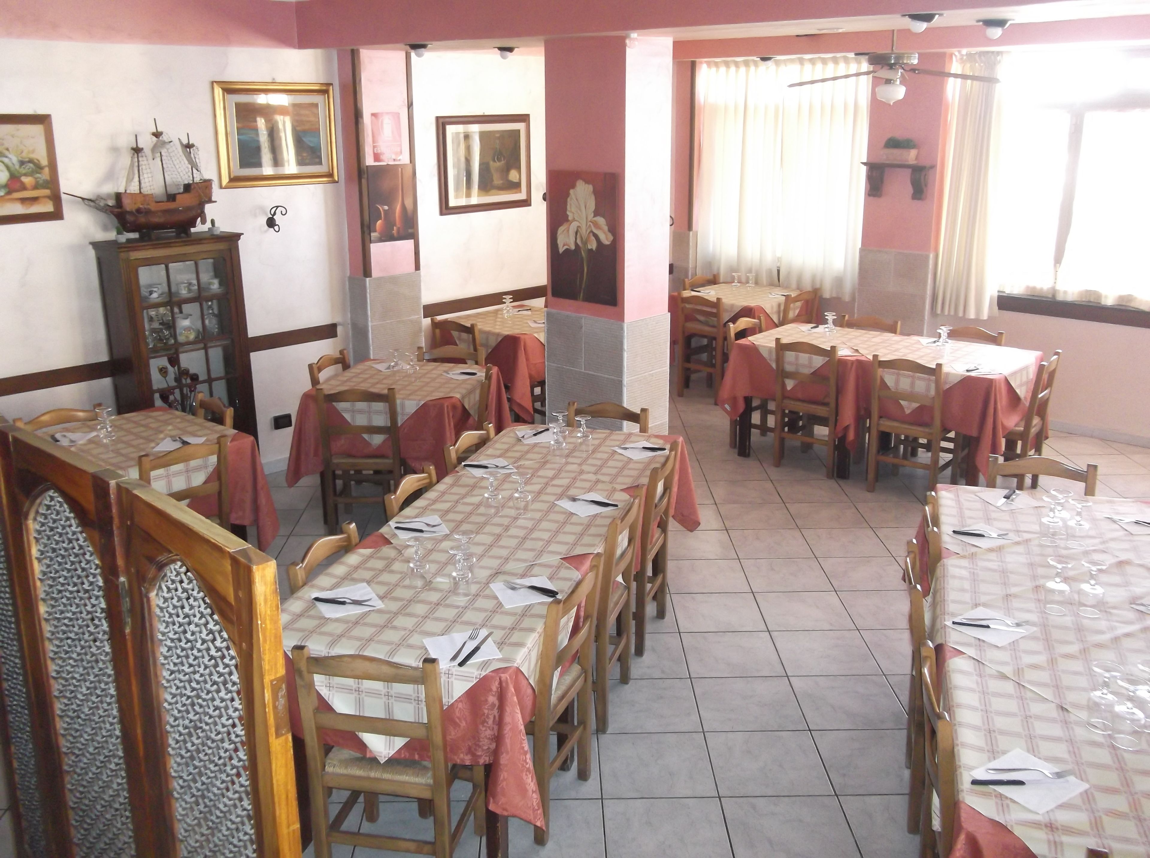 A dining area with tables set for service, wooden chairs, and a ship model on a cabinet.
