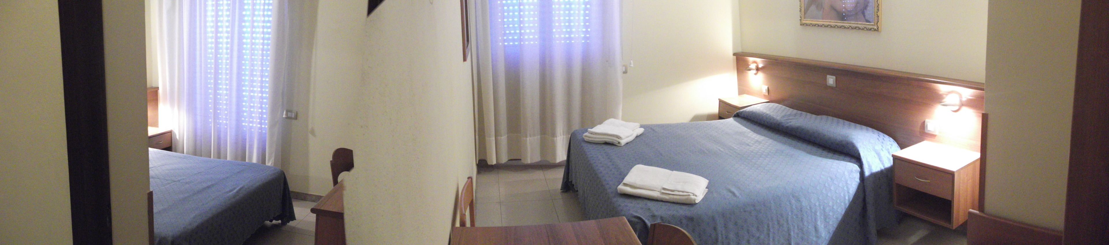 Una habitación de hotel con dos camas individuales, un cabecero de madera, una mesita de noche, una mesa y una silla.