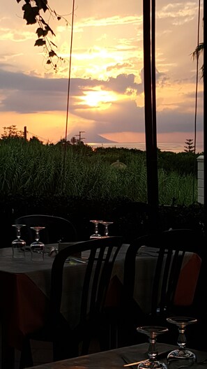 Ein Essbereich im Freien mit Tischen und Stühlen, mit Blick auf ein Feld und einen Sonnenuntergang.