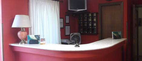 A reception area with a counter, a lamp, a television, a clock, and a fan.
