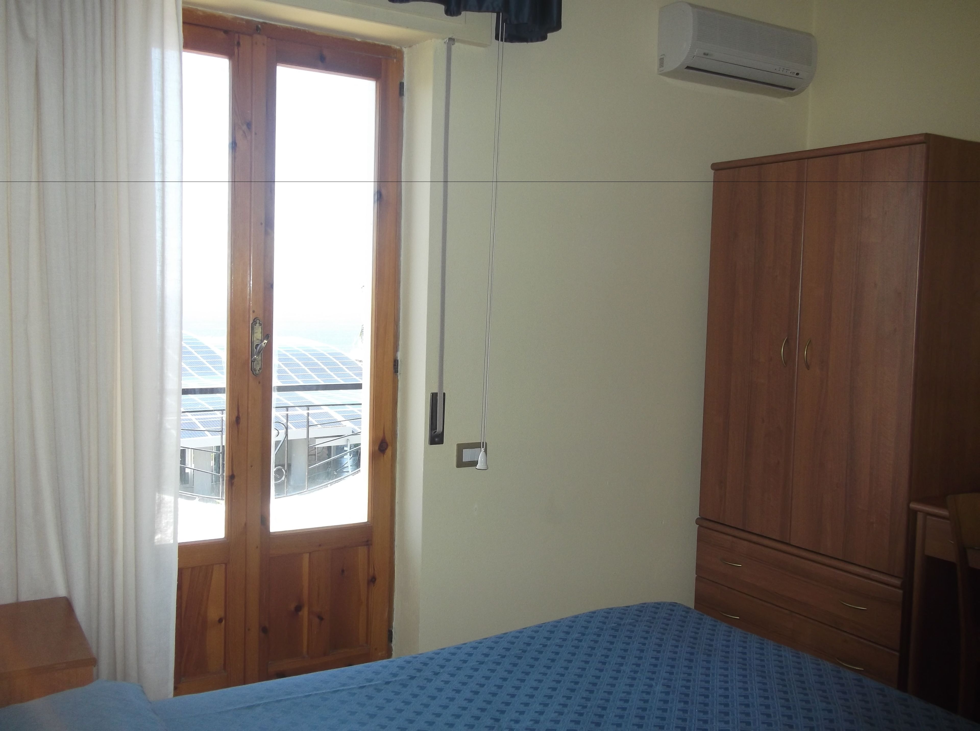 A bedroom with a bed, a wardrobe, a window with curtains, and an air conditioning unit.