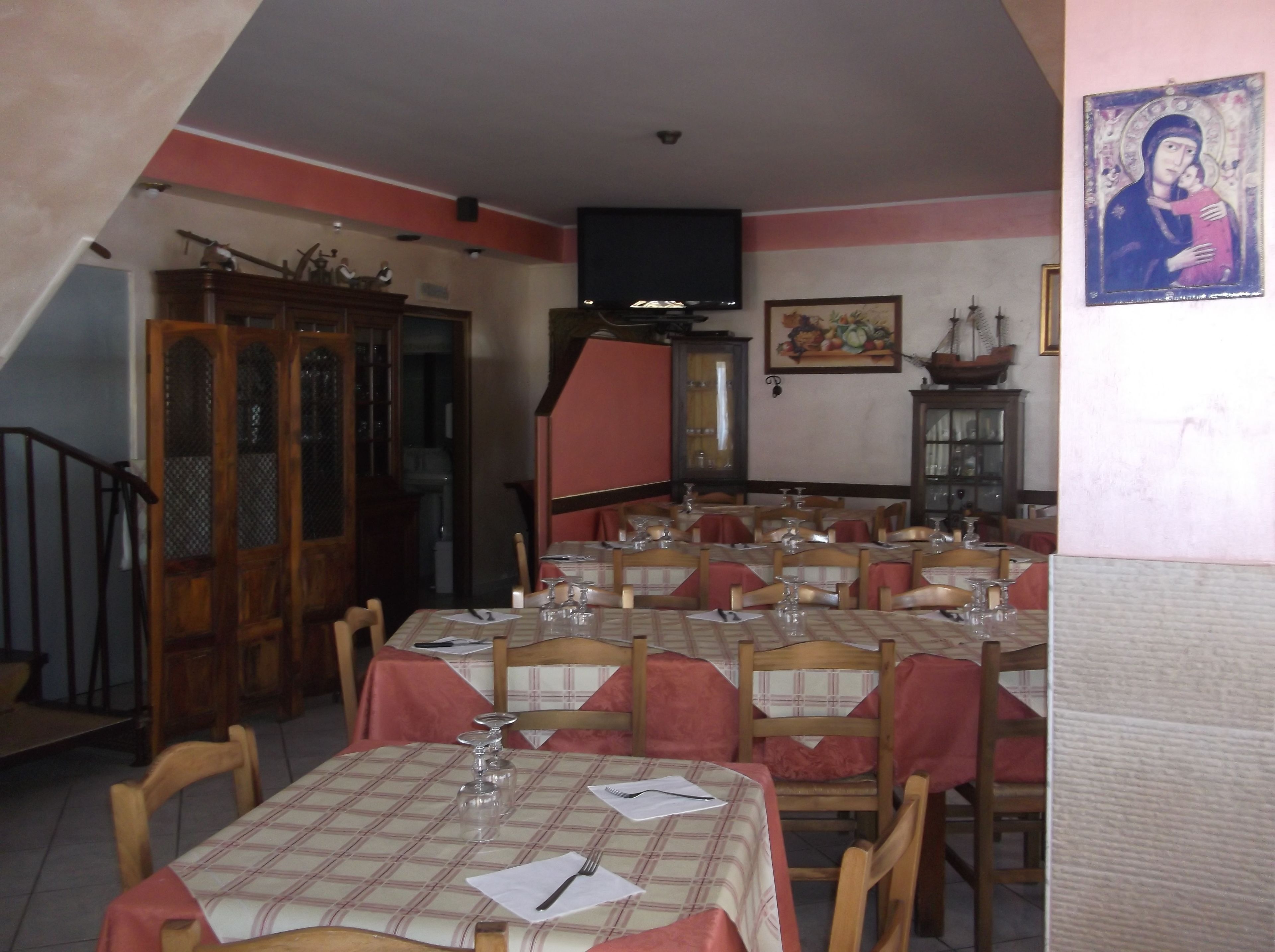 A dining area with multiple tables set for meals, a wooden cabinet, a television mounted on the wall, and a painting.