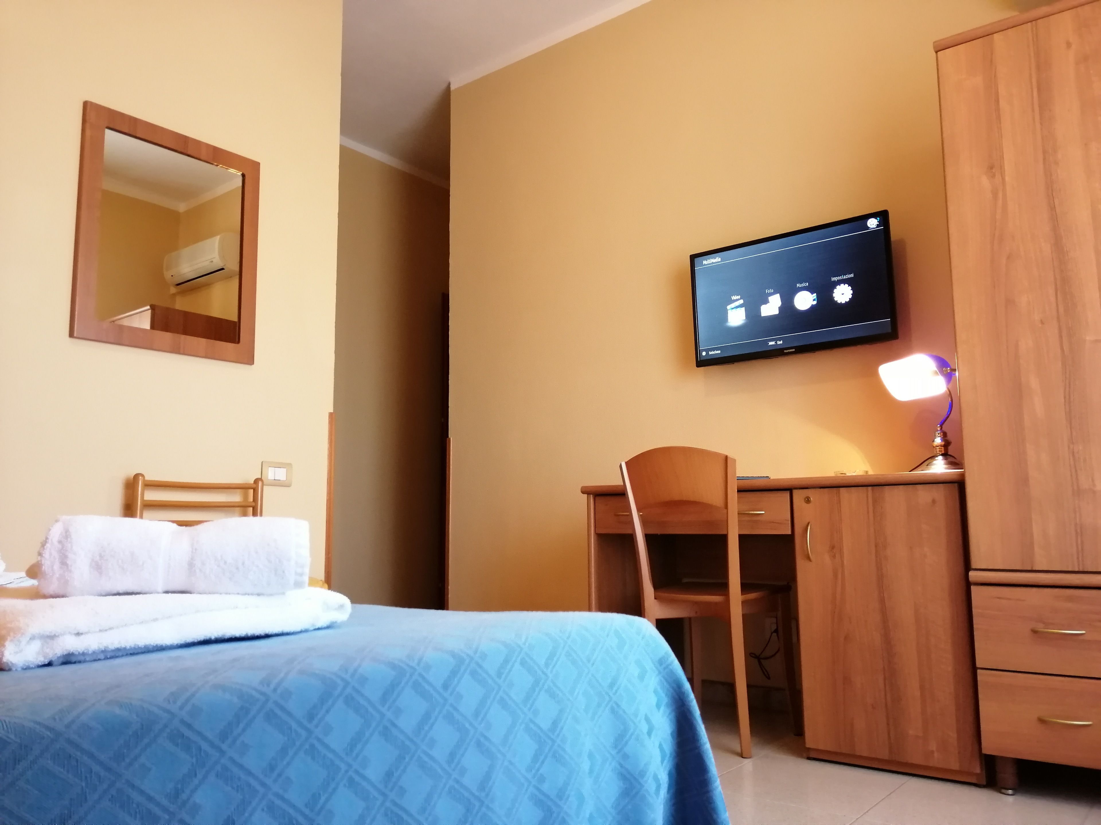 A hotel room with a bed, a desk, a chair, a wardrobe, a television, and a mirror.