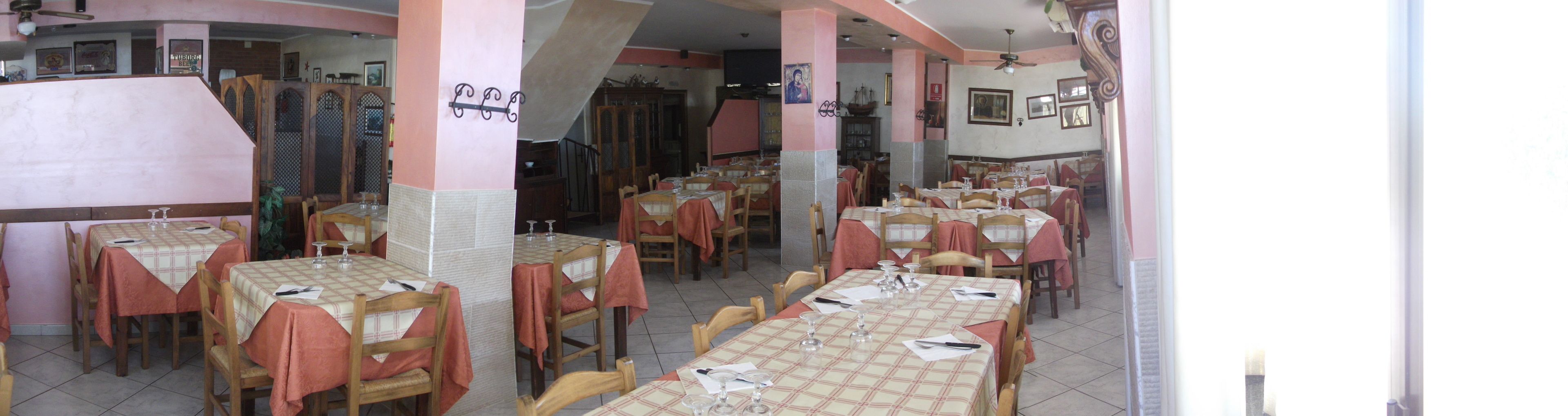 A restaurant with multiple tables and chairs, some with tablecloths. There are wooden chairs and tables, and a few tables have placemats.