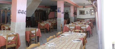 A restaurant with multiple tables and chairs, some with tablecloths. There are wooden chairs and tables, and a few tables have placemats.