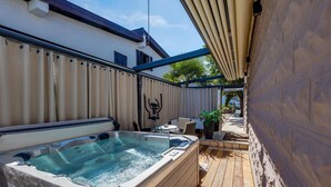 Un bain à remous situé dans un espace extérieur abrité, doté d’une terrasse en bois, d’une table, de chaises et d’une plante en pot.