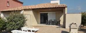 A small house with a tiled roof, a covered patio with outdoor furniture, and a gravel driveway. - Résidence Tamaris 2 (Lecci)