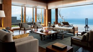 A modern living room with a view of the ocean, featuring a sofa, chairs, a coffee table, and a large window. - Six Senses Bali (Pecatu)