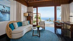 A modern living room with a curved sofa, a round coffee table, and a view of the ocean through large glass doors. - Six Senses Bali (Pecatu)