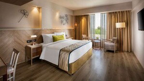 A hotel room with a large bed, a desk, a chair, a TV, and a window with curtains. - Sarovar Premiere Jaipur (Jaipur)