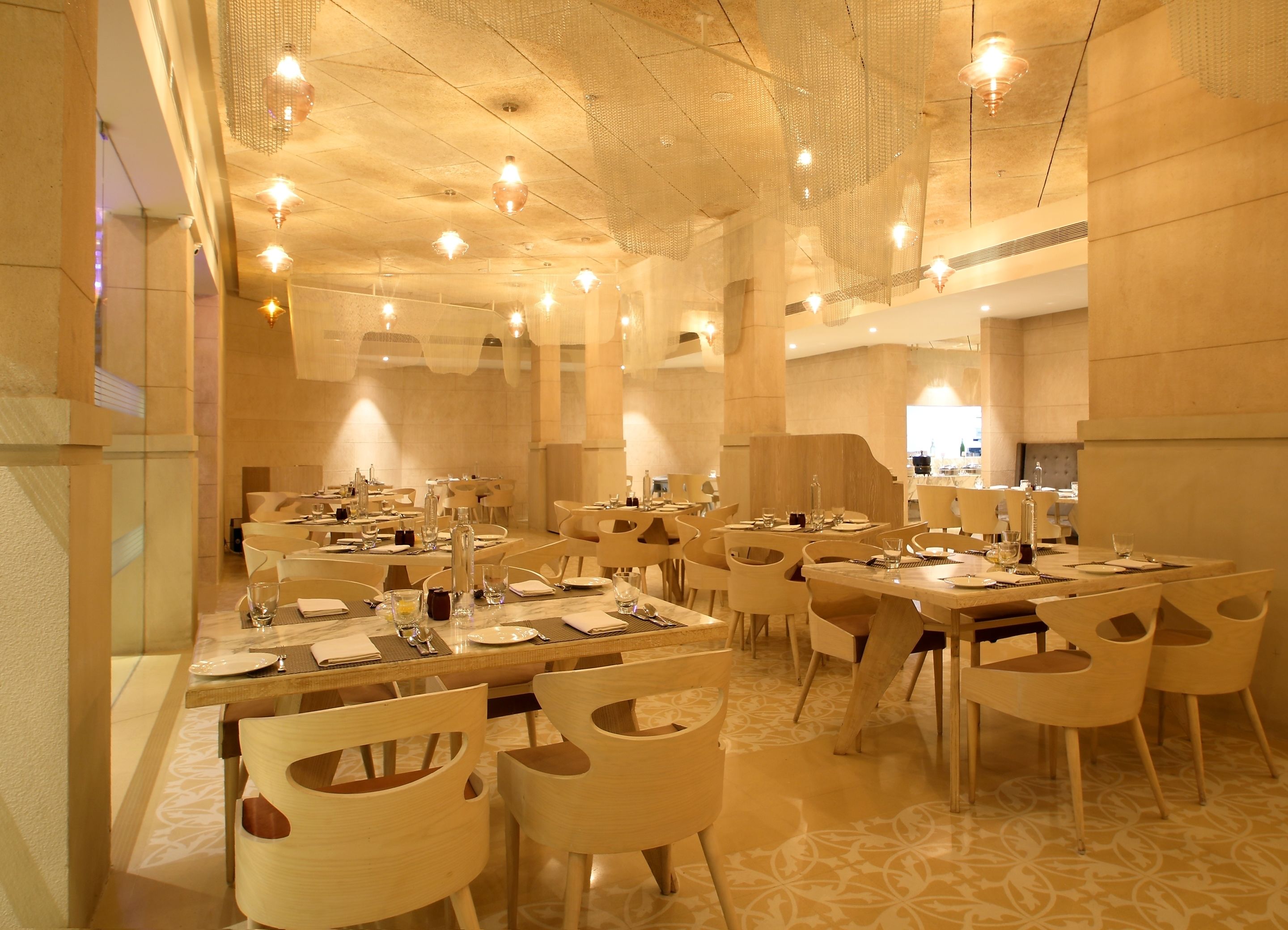 Uma ampla área de jantar com várias mesas e cadeiras, teto alto com luminárias pendentes e design arquitetônico moderno.