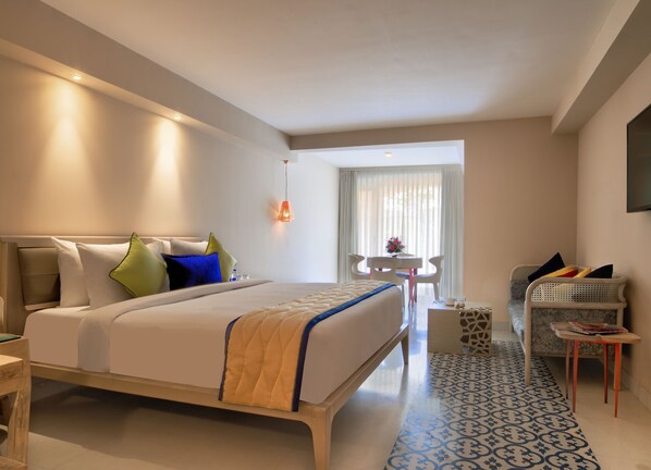 Habitación de hotel con una cama grande, una mesita con sillas, un sofá y un televisor en la pared.