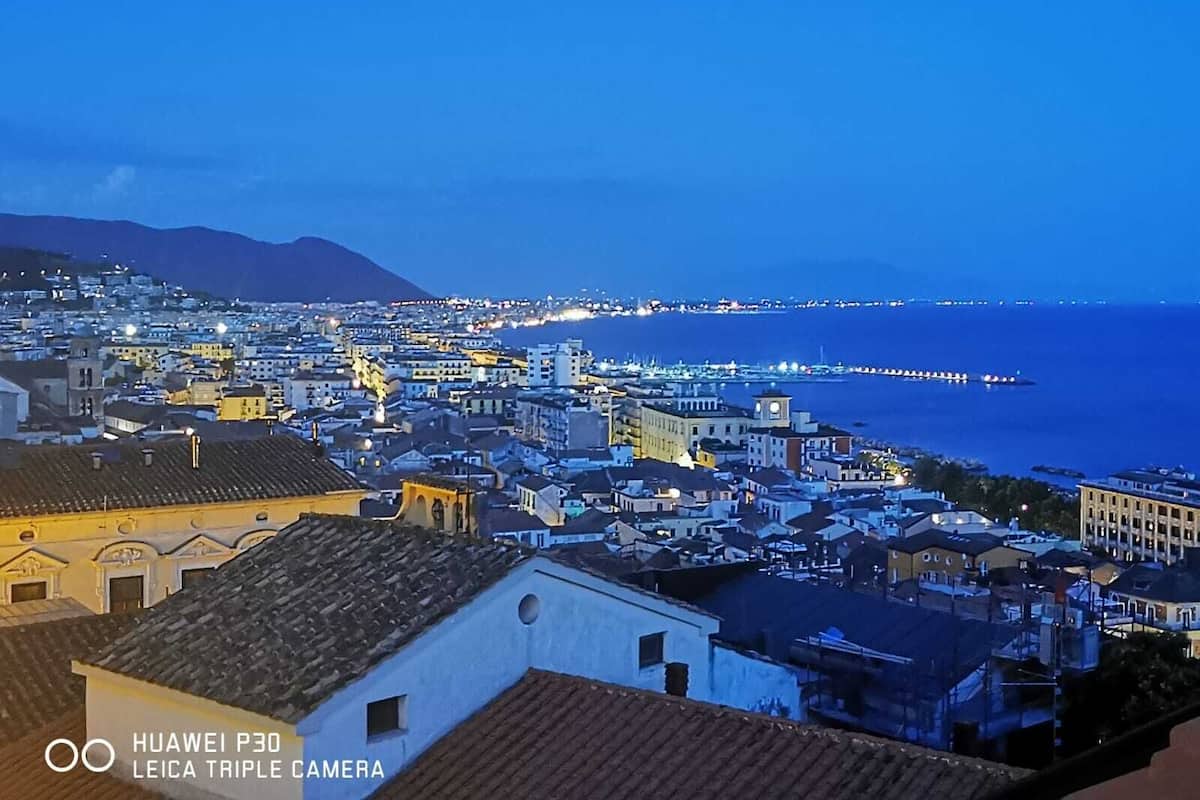 Paisagem costeira ao entardecer, com edifícios iluminados e um píer que se estende para o mar.