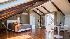 A bedroom with a sloped ceiling, a bed with a gray and orange bedspread, a round white table with chairs, and a view of the outdoors through a glass door. - Plaium Montis (Salerno)