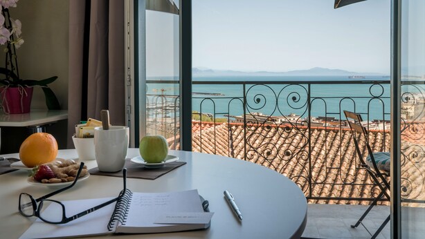 A balcony with a view of the sea and cityscape, a table with food and a notebook, and a potted orchid. - Plaium Montis (Salerno)