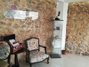 A stone wall, a floral chair, a glass display cabinet, and a small table with a book and a box. - Agartha Boutique Hotel - StoneHouse (Tomar)
