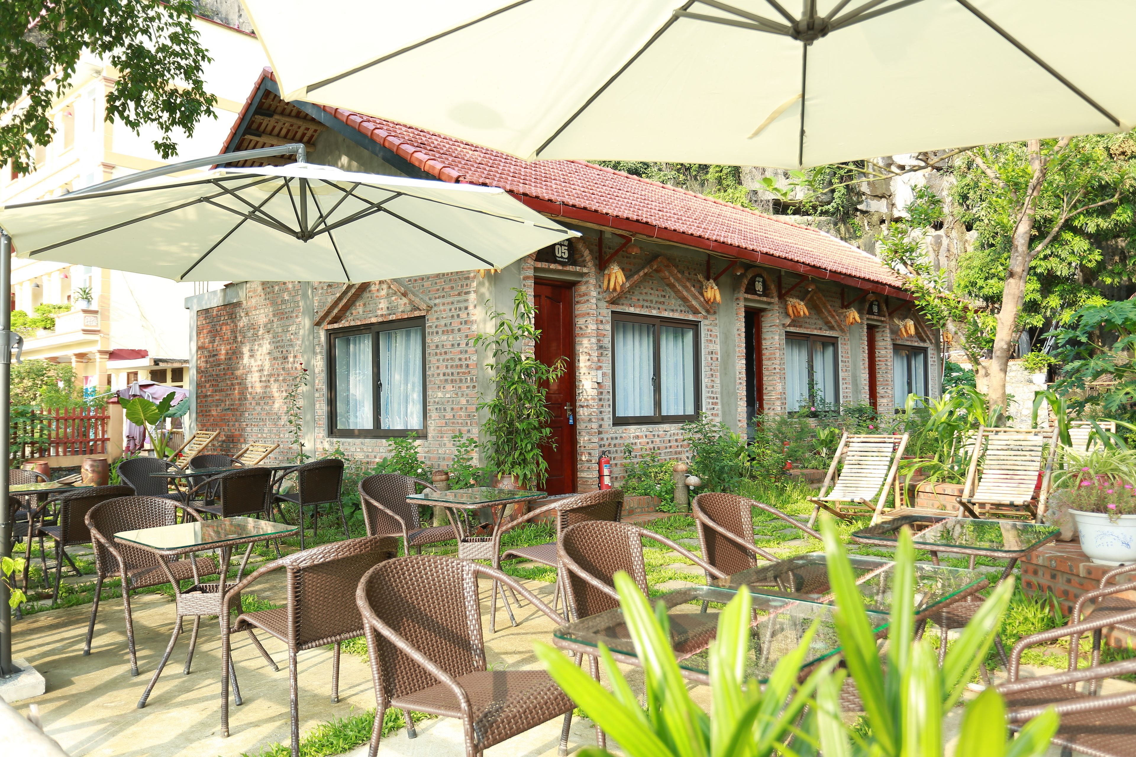 An outdoor patio with wicker chairs and tables, a brick building with a red-tiled roof, and a large umbrella providing shade.