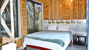 A bedroom with a large bed, wooden walls, a window with a view of trees, and a patterned tile backsplash. - Tam Coc Lakeside Homestay (Nam Hoa Lu)