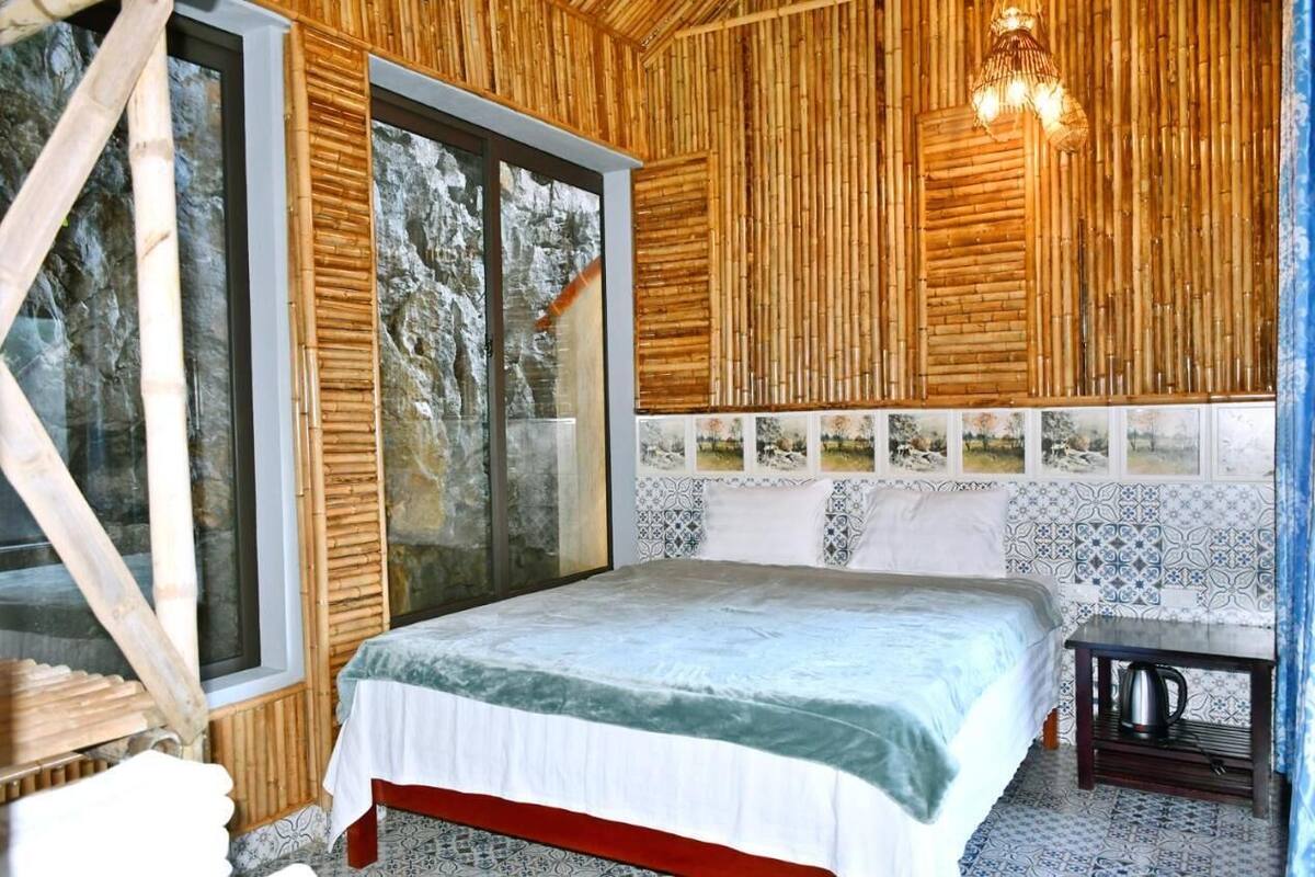 Un dormitorio con una cama grande, paredes de madera, una ventana con vista a árboles y un salpicadero de azulejos estampados.