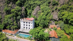 A multi-story hotel with a swimming pool, surrounded by lush greenery and rocky cliffs. - Tam Coc Lakeside Homestay (Nam Hoa Lu)