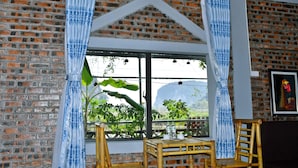 A room with a brick wall, a window with blue curtains, a wooden chair, and a table with a bottle and cup. - Tam Coc Lakeside Homestay (Nam Hoa Lu)