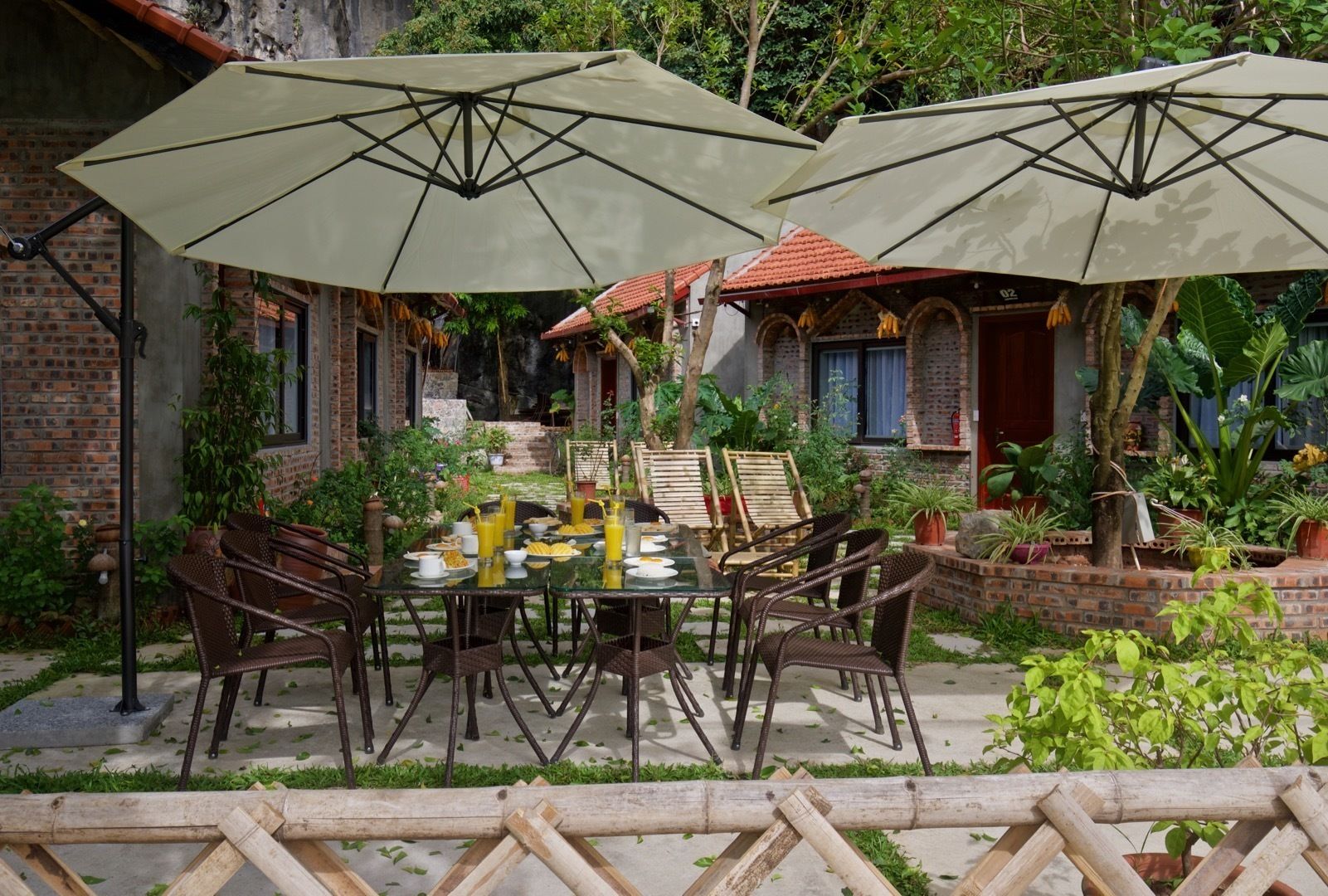 An outdoor dining area with a brick wall, potted plants, and a table set with plates, bowls, and glasses.