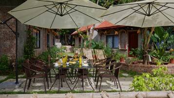 An outdoor dining area with a brick wall, potted plants, and a table set with plates, bowls, and glasses.
