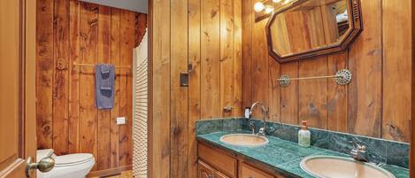 Un baño revestido de paneles de madera con dos lavamanos, un espejo con luces y un perchero para toallas.