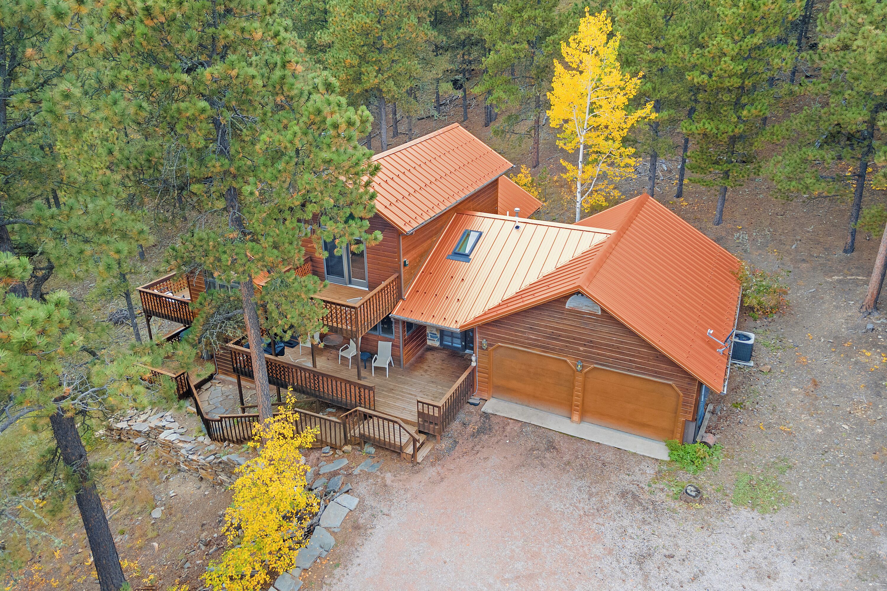 A two-story cabin with a wooden deck, a garage, and a small outdoor seating area.