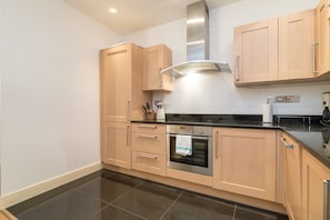 A modern kitchen with light wood cabinets, a stainless steel oven, and a black countertop.