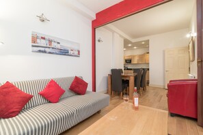 A modern living room with a striped sofa, red cushions, a dining area with a wooden table and chairs, and a kitchen in the background.