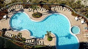 Vista aérea de una piscina de diseño curvo, rodeada de sillas de descanso y palmeras.