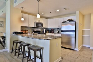 A modern kitchen with a central island, bar stools, stainless steel appliances, and pendant lighting.
