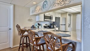 A kitchen with a central island, bar stools, a microwave, and a clock on the wall.
