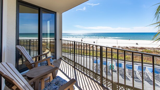 A balcony with wooden chairs and a view of the beach.