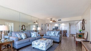 A spacious living room with a large sectional sofa, a matching ottoman, and a dining area with a wooden table and chairs.