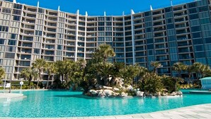 A hotel with a large pool area, surrounded by palm trees and a rocky island.