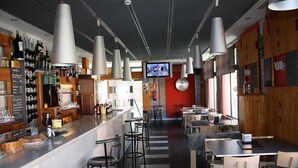A modern bar area with a counter, bar stools, and a television screen. - Hotel Castillo del Alba (Somiedo)