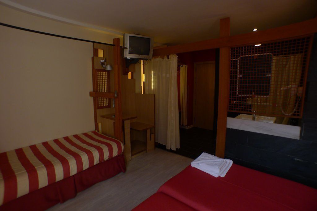 A hotel room with two beds, a TV, a small table, and a window with curtains.