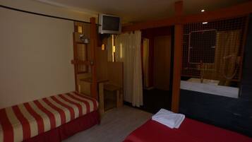 A hotel room with two beds, a TV, a small table, and a window with curtains.