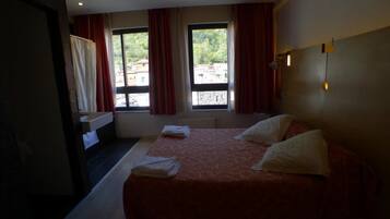 Een hotelkamer met een groot bed, twee ramen met gordijnen, een nachtkastje en uitzicht op de omgeving.
