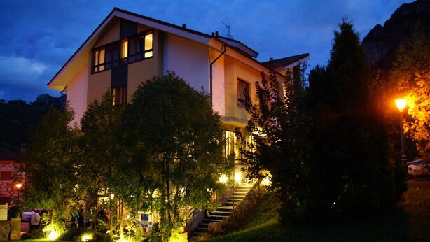 A two-story house with a balcony, surrounded by trees and a mountain in the background. - Hotel Castillo del Alba (Somiedo)