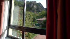 A window with a view of a mountainous landscape and a building with a red roof. - Hotel Castillo del Alba (Somiedo)