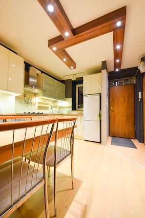 Une cuisine moderne avec des poutres en bois, un réfrigérateur et un coin bar avec des chaises en métal.