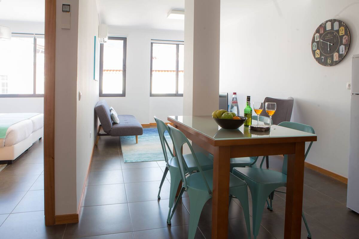 Una sala de estar moderna con un sofá, una mesa de comedor con sillas, un reloj en la pared y una ventana.
